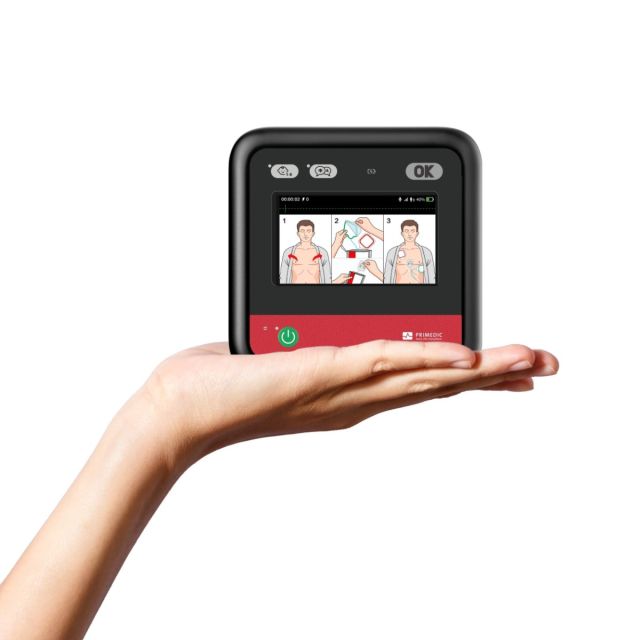 Primedic HeartSave myPAD fully automatic AED held in one hand, showing compact 15 x 15cm black and red device with colour LCD display