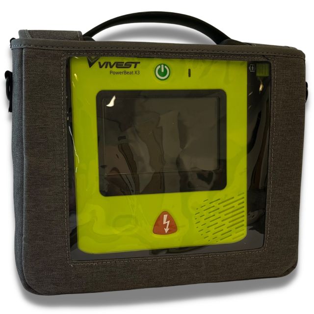 A grey, fabric carry case with a carry handle containing the Vivest Power Beat X3 defibrillator. The carry case has a huge, clear viewing window so you can see the majority of the defibrillator inside and the LED screen it has.