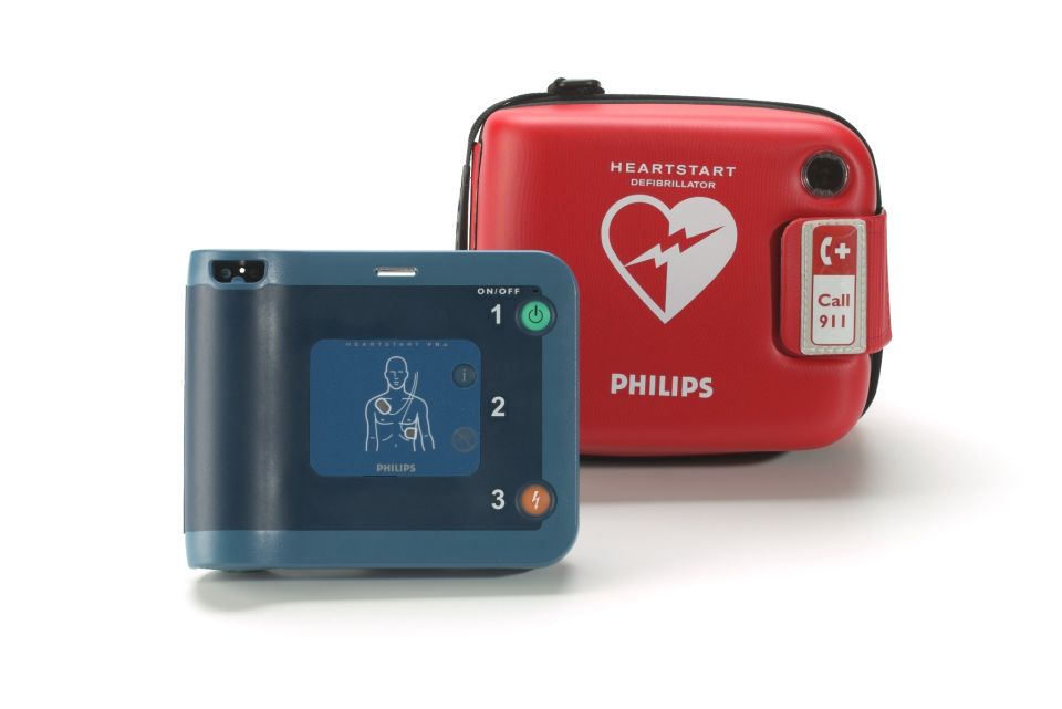 Semi-automatic Philips Heartstart FRx defibrillator next to standard carry case showing Philips logo and anatomical diagram for electrode pad placement