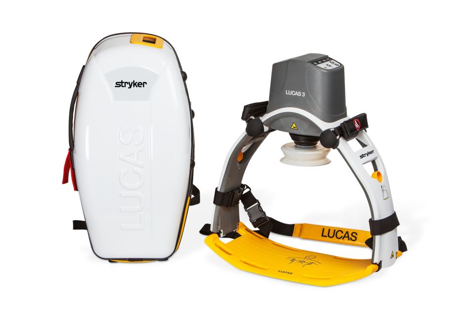 Hard, rigid carry case for wearable automatic chest compression device, with a battery viewing window. A white, angular backpack with yellow accents and rugged shoulder straps. Placed next to the Stryker Lucas 3.1 chest compression system.